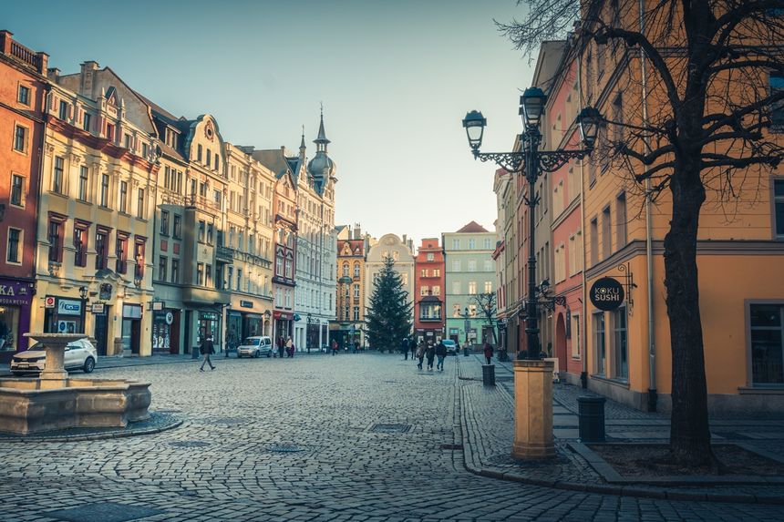 Świdnica. Ulica z kolorowymi kamienicami, świąteczna choinka, ludzie spacerujący, jasne niebo.