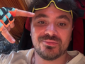 Daniel Martyniuk w kolorowych rękawicach, z uśmiechem i okularami, pokazuje znak pokoju.