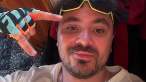 Daniel Martyniuk w kolorowych rękawicach, z uśmiechem i okularami, pokazuje znak pokoju.