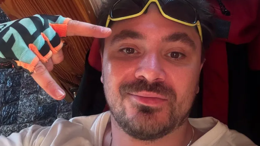 Daniel Martyniuk w kolorowych rękawicach, z uśmiechem i okularami, pokazuje znak pokoju.