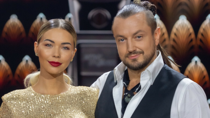 Sandra Kubicka i Aleksander Baron w eleganckich strojach na tle jasnej dekoracji.