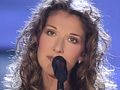 Céline Dion z kręconymi, długimi włosami, śpiewająca do mikrofonu.