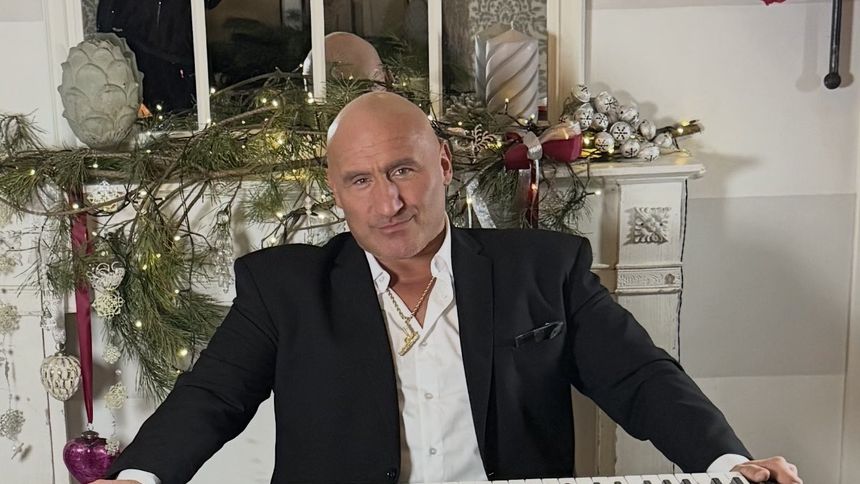 Marcin Najman w garniturze gra na keyboardzie, w tle świąteczne dekoracje.