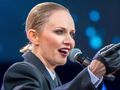 Kobieta w czarnym garniturze, z mikrofonem, śpiewa na scenie w blasku świateł.