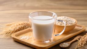 Szklanka mleka na drewnianej podstawce, obok talerz z płatkami owsianymi.