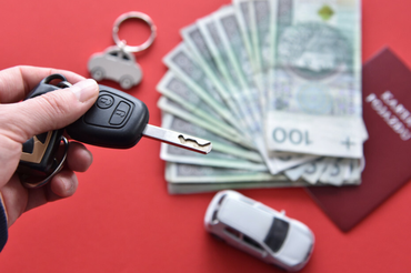 Kluczyki do auta, w tle pieniadze, zabawkowe auto, karta pojazdu i breloczek - materiał poglądowy