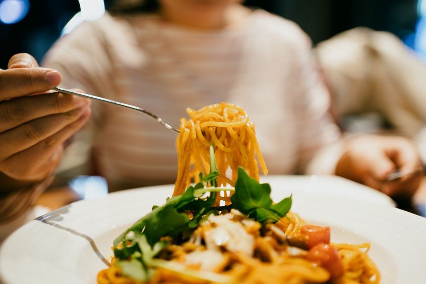 Na talerzu makaron spaghetti z ziołami. Ktoś z widelcem nabiera porcję.