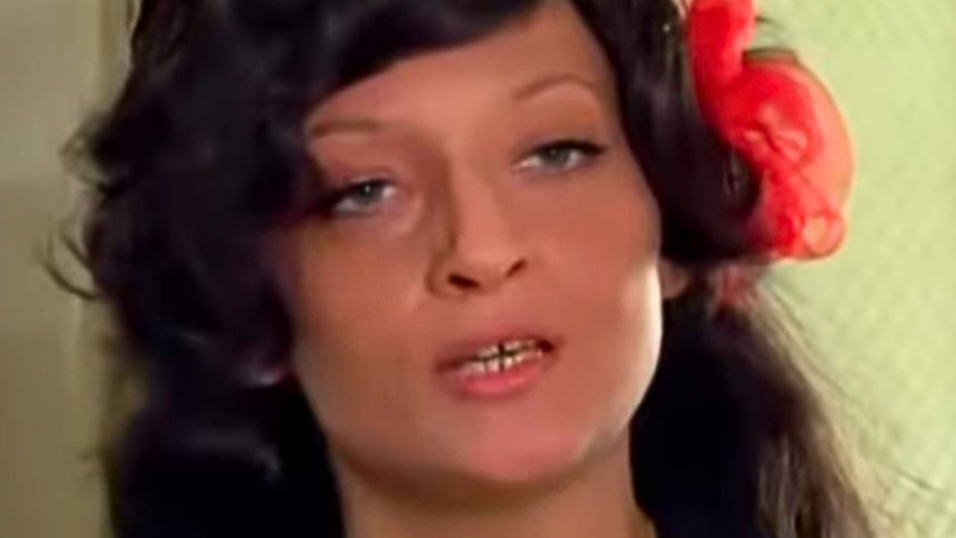 Na zdjęciu widoczna jest kobieta z ciemnymi, długimi włosami i czerwoną dekoracją we włosach.