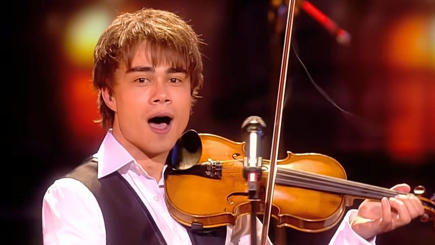 Alexander Rybak gra na skrzypcach, uśmiechając się do widowni. Jest w białej koszuli.