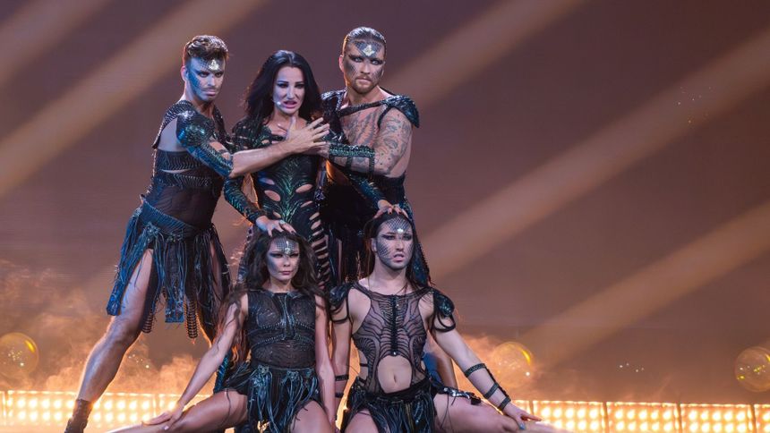 Grupa tancerzy w kostiumach, prezentujących dynamiczną choreografię na scenie.