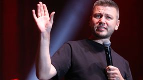 Mateusz Socha w czarnej koszulce trzyma mikrofon i gestykuluje, stojąc na scenie.