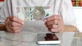 Smartfon na stole, pieniądze w dłoni