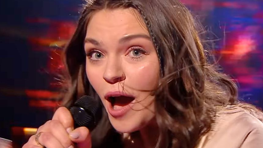 Młoda kobieta z mikrofonem, wyrażająca emocje, z rozwianymi włosami na kolorowym tle.