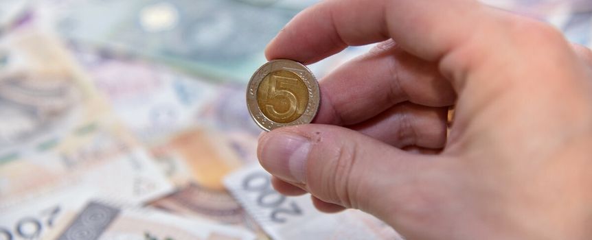 5 zł w palcach na tle banknotów