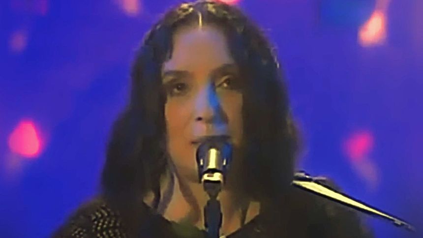 Kobieta z długimi, ciemnymi włosami śpiewa do mikrofonu na kolorowej scenie.