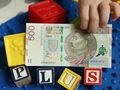 500 zł w rękach dziecka i napis "plus" z klocków