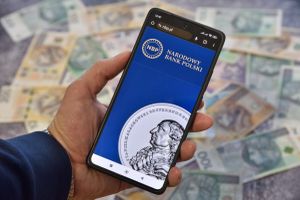 smartfon ze stroną NBP na tle pieniędzy