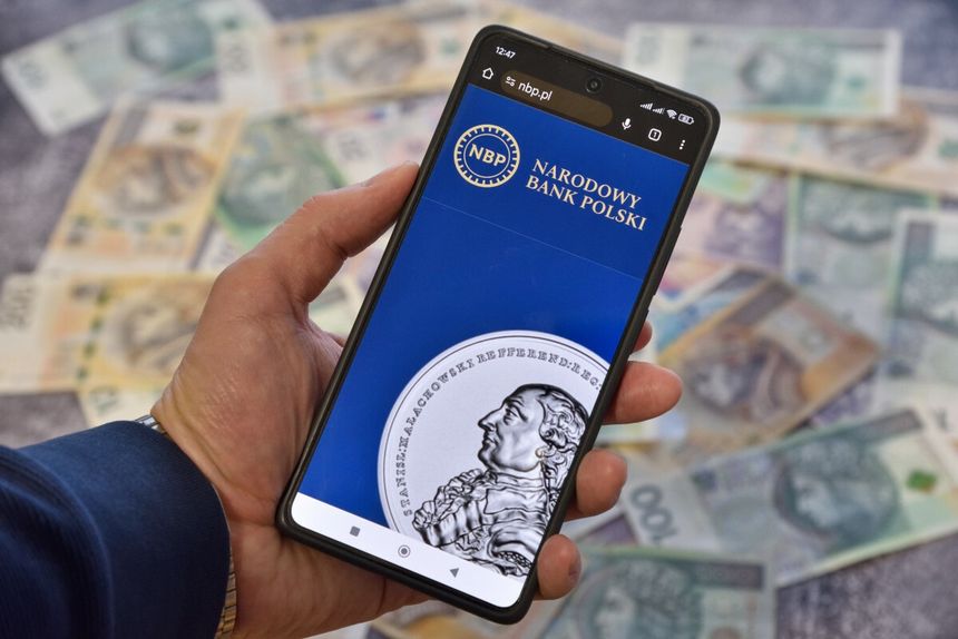 smartfon ze stroną NBP na tle pieniędzy