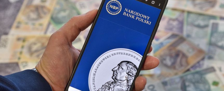 smartfon ze stroną NBP na tle pieniędzy