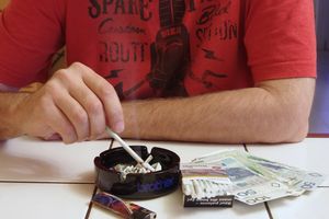 mężczyzna strzepujący papierosa do popielniczki obok pieniędzy