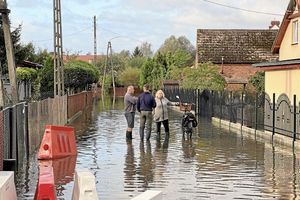 trzy osoby stojące na zalanej wodą ulicy między domami