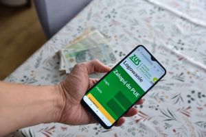 ZUS PEU na smartfonie na tle pieniędzy na stole