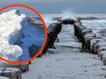 Na plaży widoczna drewniana falochron, w tle morskie fale i fragment lodu. Pochmurne niebo.