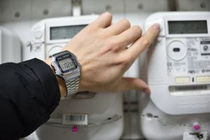 ręką z zegarkiem na tle liczników prądu elektrycznego