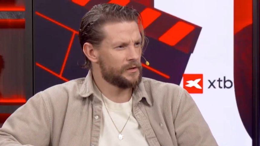 Sebastian Fabijański siedzi przed mikrofonem, wyrażając zaskoczenie.