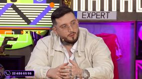 Michał „Boxdel” Baron w jasnej kurtce i okularach, siedzi przy stole, gestykulując podczas rozmowy.