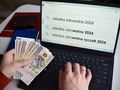 mężczyzna z pieniędzmi przed komputerm z napisem składka zdrowotna 2024 na ekranie