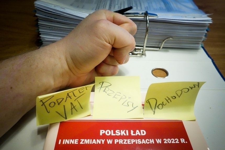 zaciśnięta pięść i karteczki z napisami podatek VAT, dochodowy, polski ład