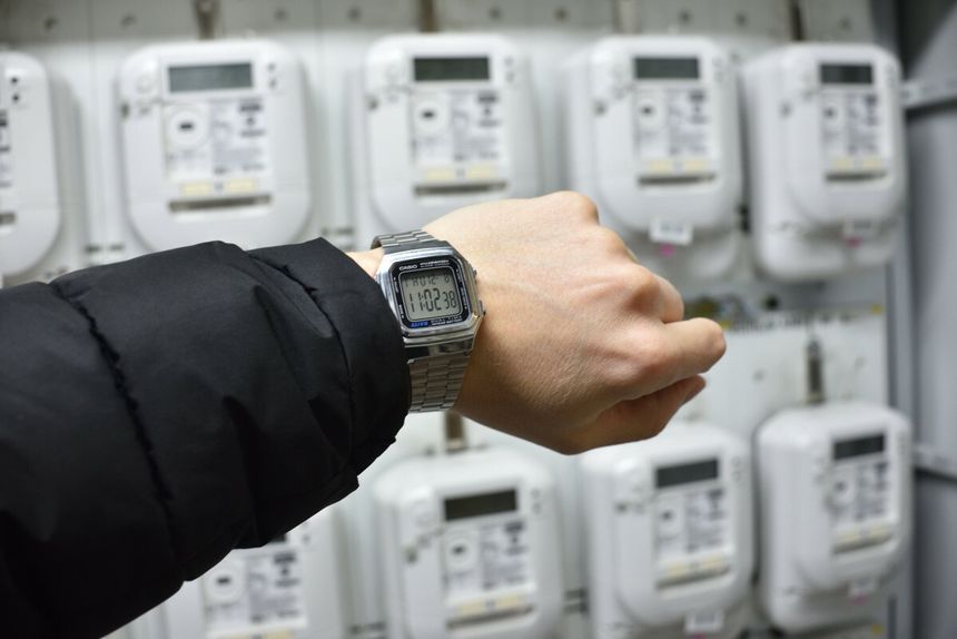 ręka z zegarkiem na tle liczników energii elektrycznych