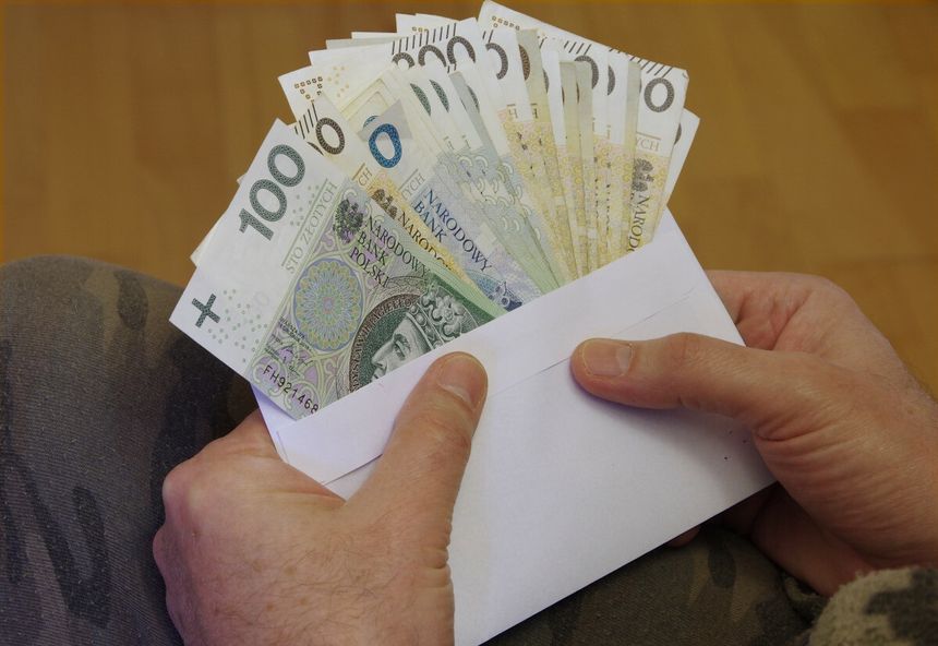 mężczyzna trzymający kopertę z wystającymi pieniędzmi