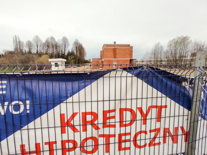 baner o kredytach hipotecznych rozwieszony na ogrodzeniu budowy