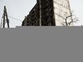 kobieta przechodząca przed zniszczonym blokiem mieszkalnym w Mariupolu