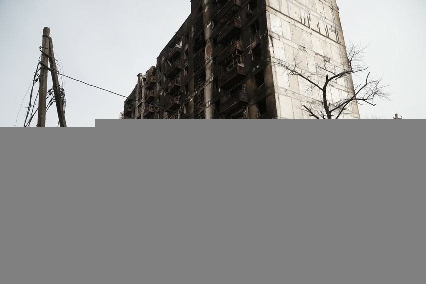 kobieta przechodząca przed zniszczonym blokiem mieszkalnym w Mariupolu