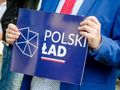 mężczyzna w garniturze trzymający tabliczkę z Polskim Ładem