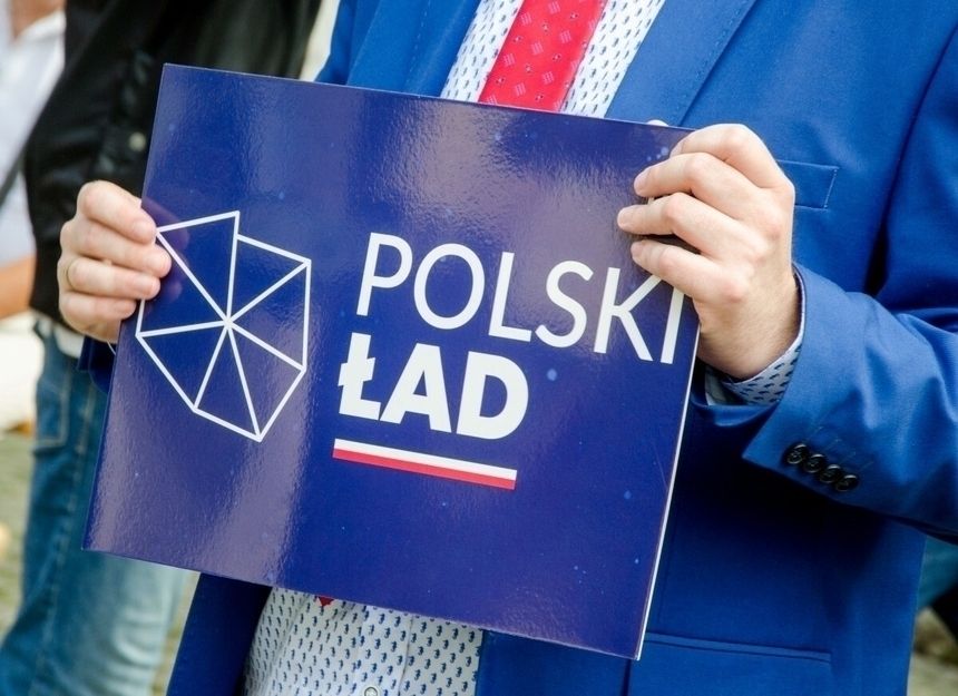 mężczyzna w garniturze trzymający tabliczkę z Polskim Ładem