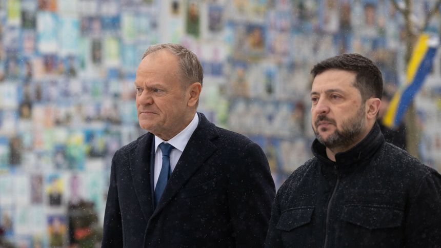 Dwóch mężczyzn w zimowych kurtkach, spacerujących w śniegu, tło z plakatami. Donald Tusk z lewej.