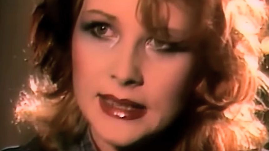  Kobieta z kręconymi włosami i wyrazistym makijażem, przybliżona twarz.