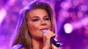 Kobieta z mikrofonem, śpiewająca na tle kolorowych świateł.