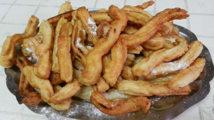 Żółte, chrupiące ciastka w formie spirali, posypane cukrem pudrem na metalowym talerzu.