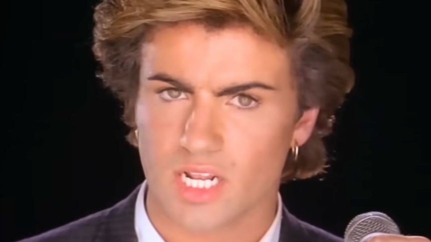 Mężczyzna z krótkimi, falującymi włosami, trzyma mikrofon i śpiewa, wyrażając emocje.