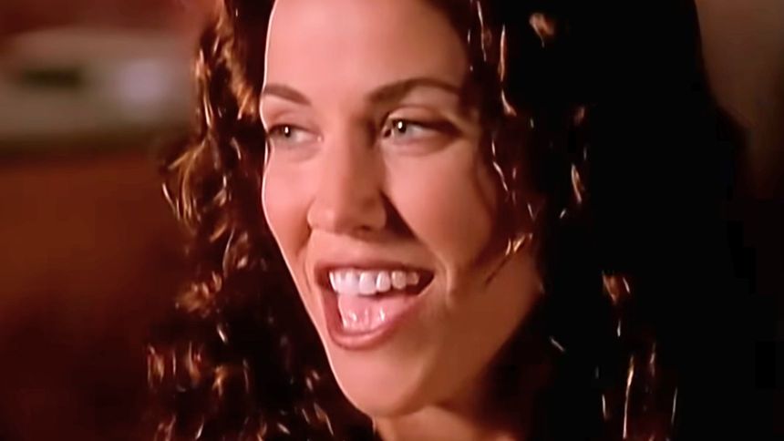 Na zdjęciu uśmiechnięta kobieta z kręconymi włosami, opowiada coś z entuzjazmem.