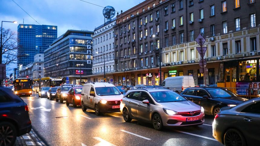 Zatłoczona ulica w mieście, oświetlone budynki i zaparkowane samochody w zmierzchu