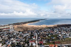 Widok na nadmorską miejscowość, pola, morze i niebo z chmurami. W tle wybrzeże i las