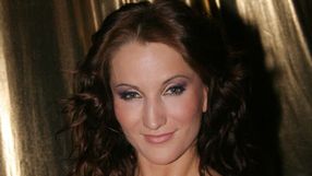 Justyna Steczkowska z kręconymi włosami, uśmiechająca się na tle złotej tkaniny.