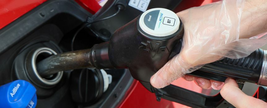Osoba w rękawiczkach tankuje samochód na stacji paliw, widoczne paliwo typu diesel.