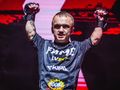 Mini Majk w sportowym stroju FAME, unosi ręce w geście zwycięstwa na tle intensywnego światła.